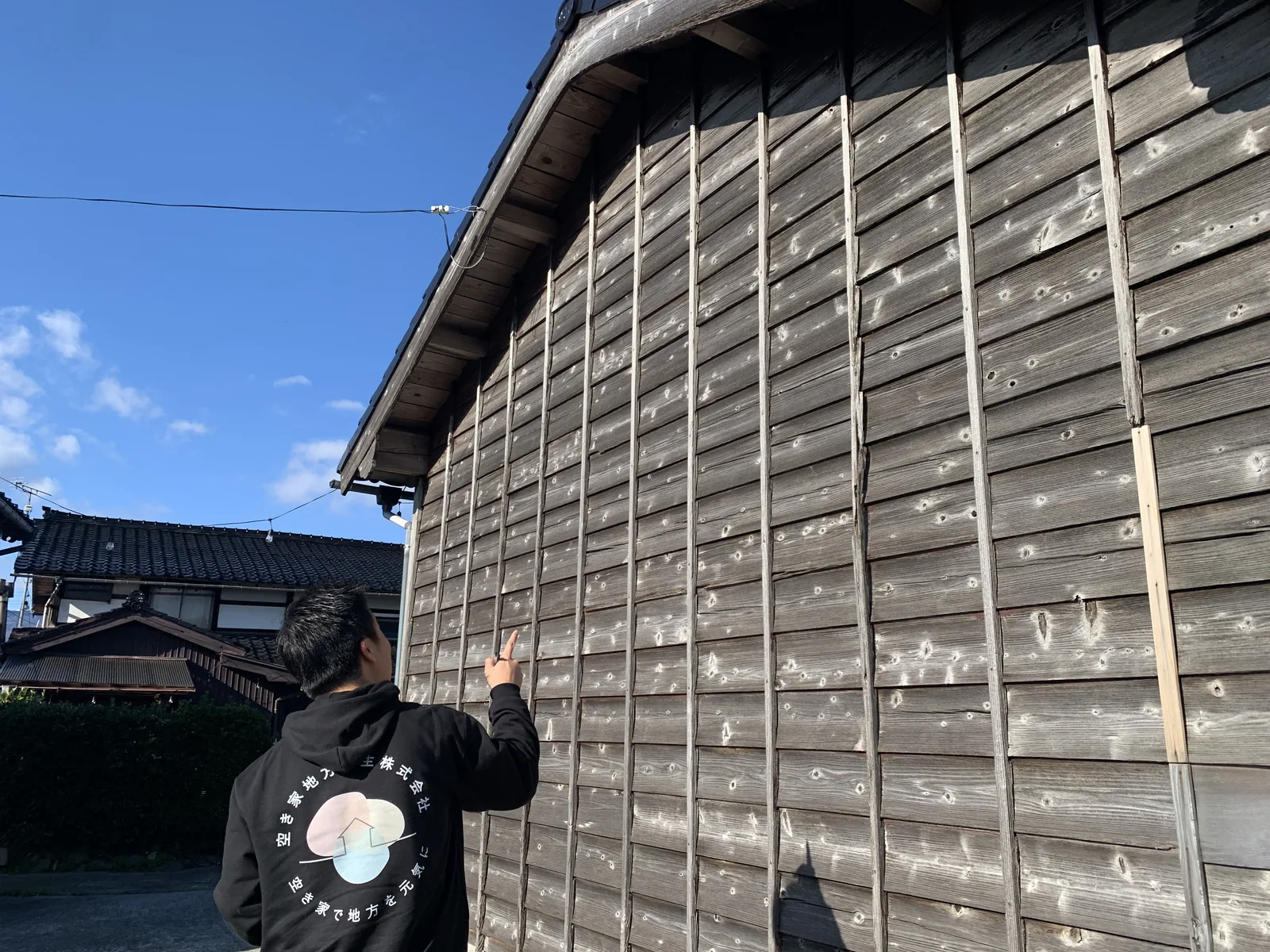 空き家の外壁を指さして傷み具合を確認するスタッフ